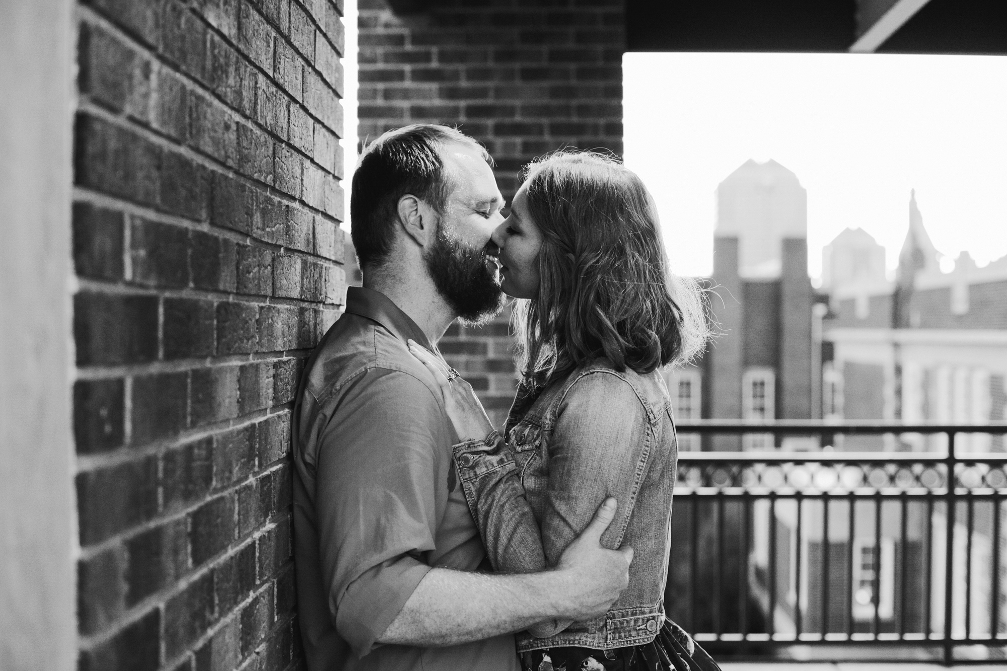 The couple by a brick wall with the city in the background. 