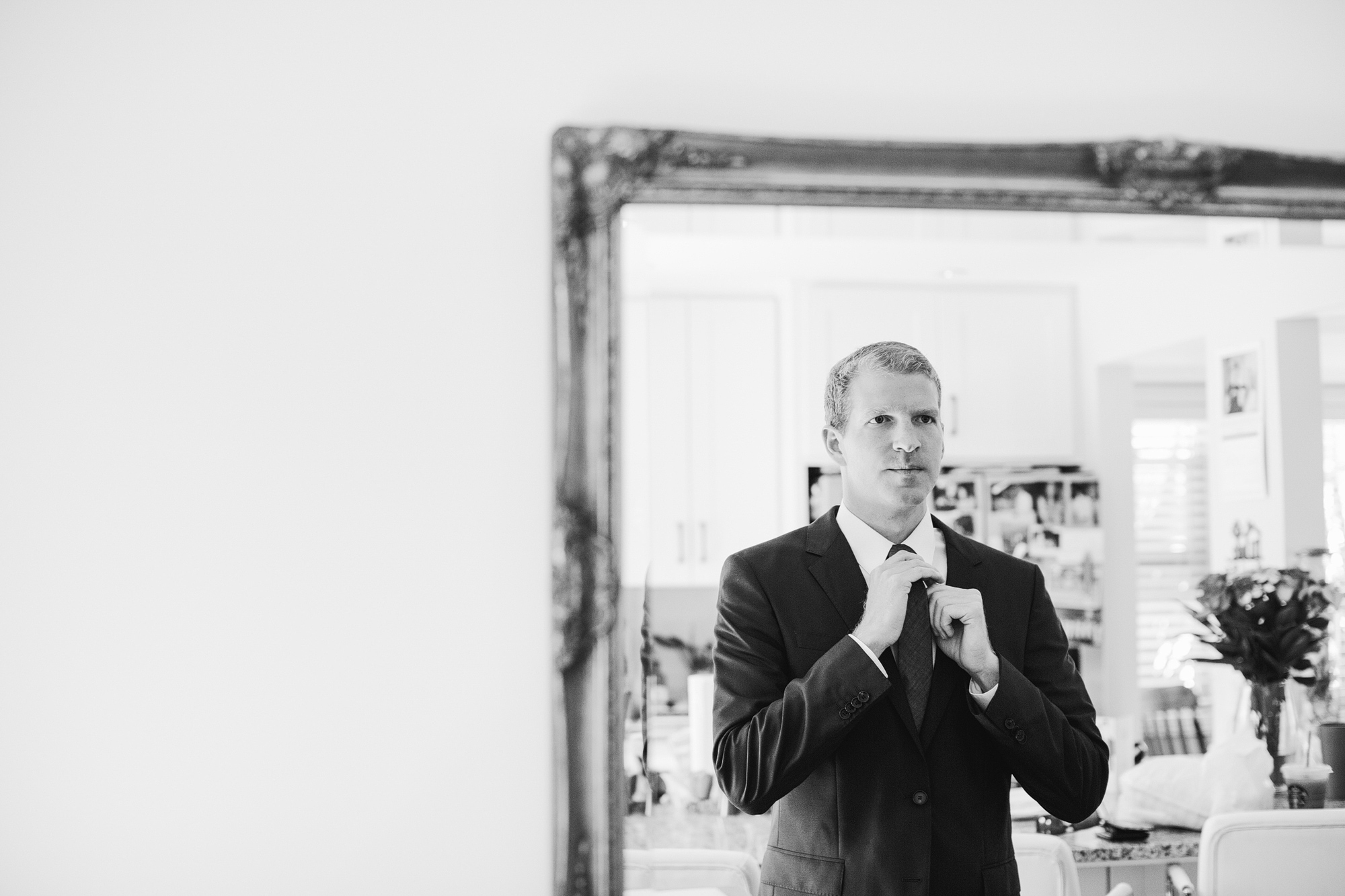 The groom adjusting his tie in the mirror. 