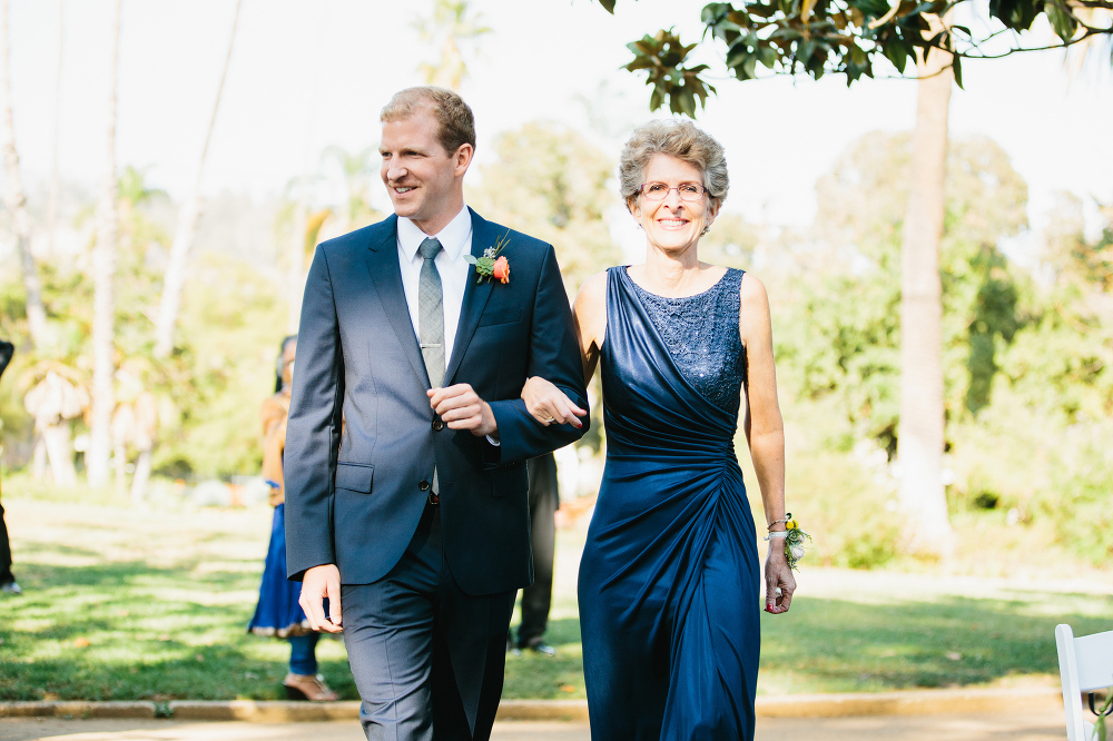 The groom walking down the aisle with his mom. 