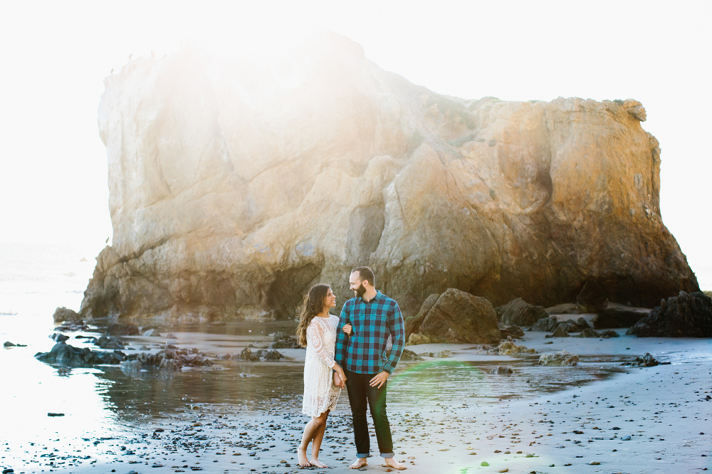 The couple in front of a large rock on the beach. 