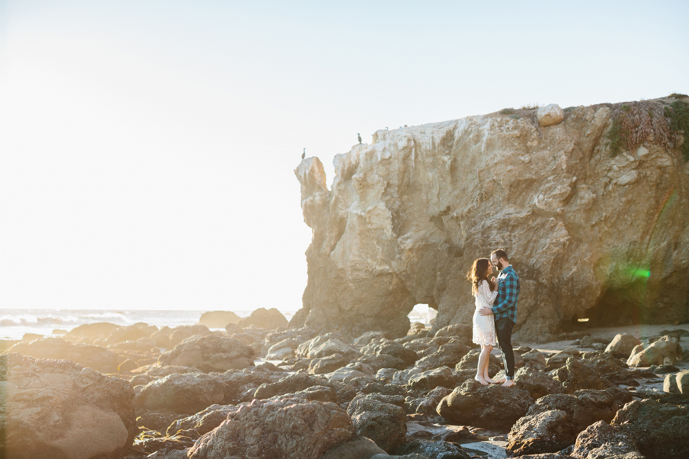 The couple standing on rocks on the beach. 