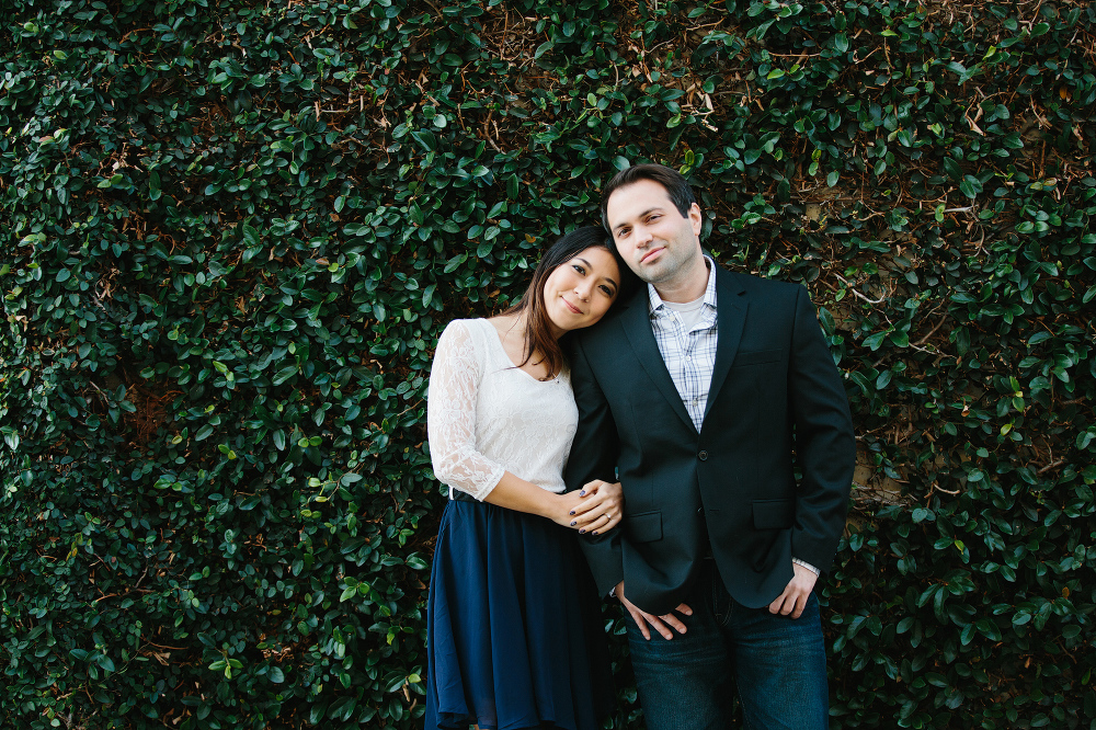 The couple standing in front of green vine wall. 