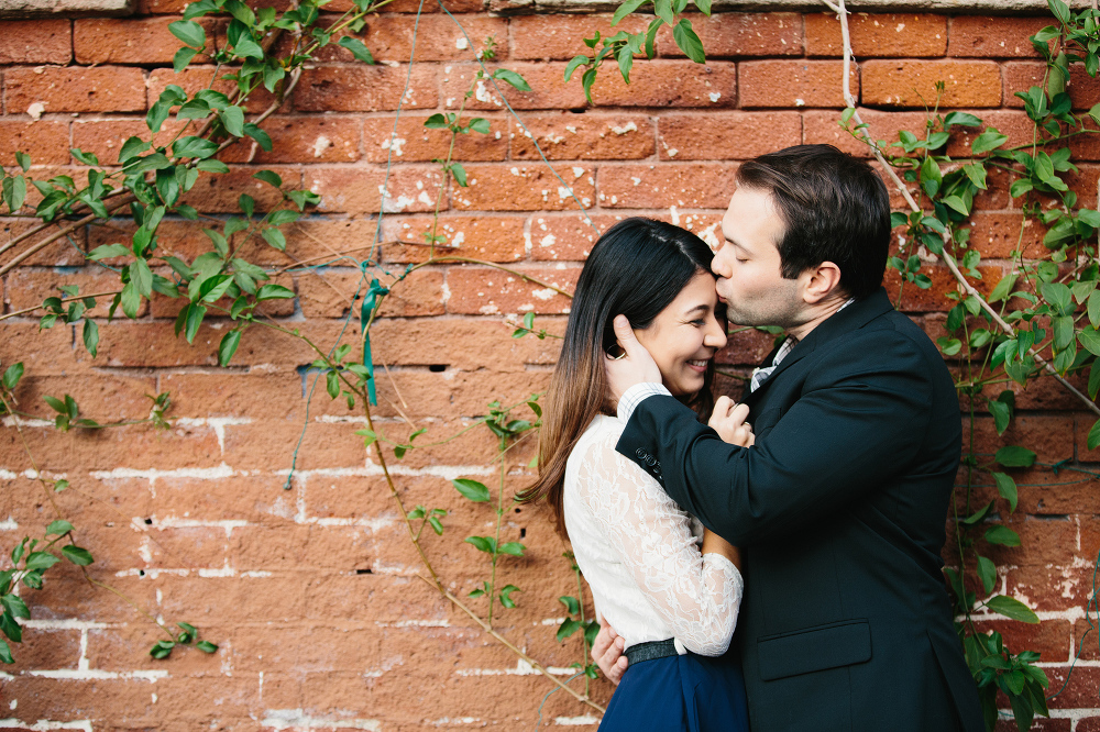 The couple in front of brick wall with vines. 