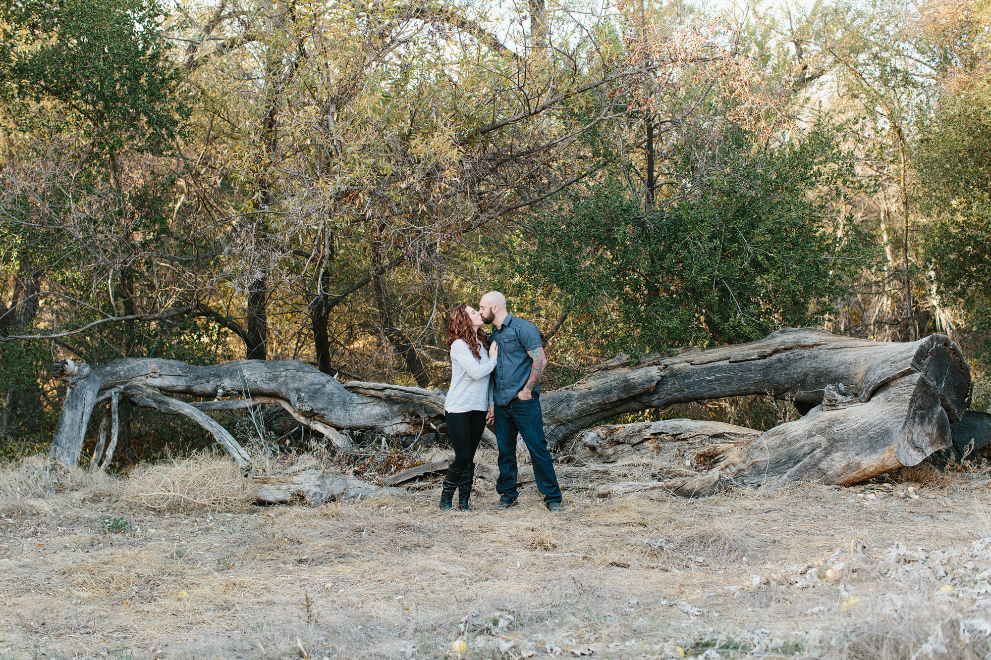 The couple standing in front of a large fallen tree. 