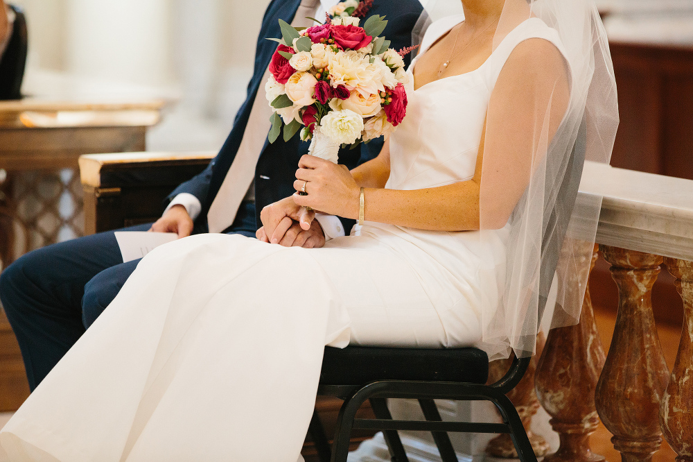 The bride and groom sitting together holding hands during the mass. 