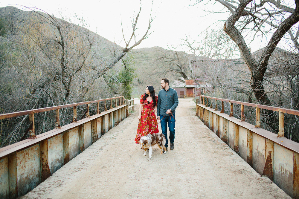 The couple walking their dog on a bridge. 