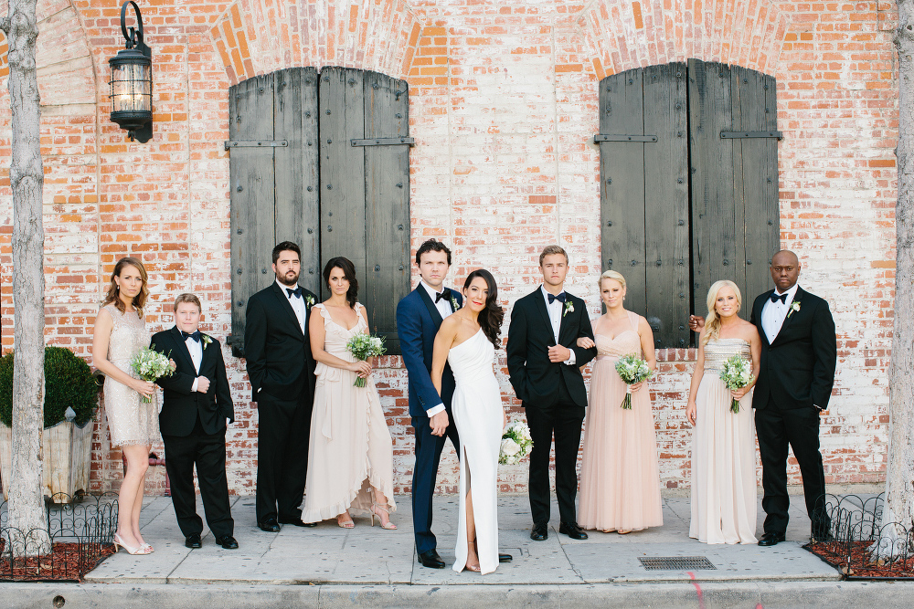 The full wedding party in front of a brick wall. 