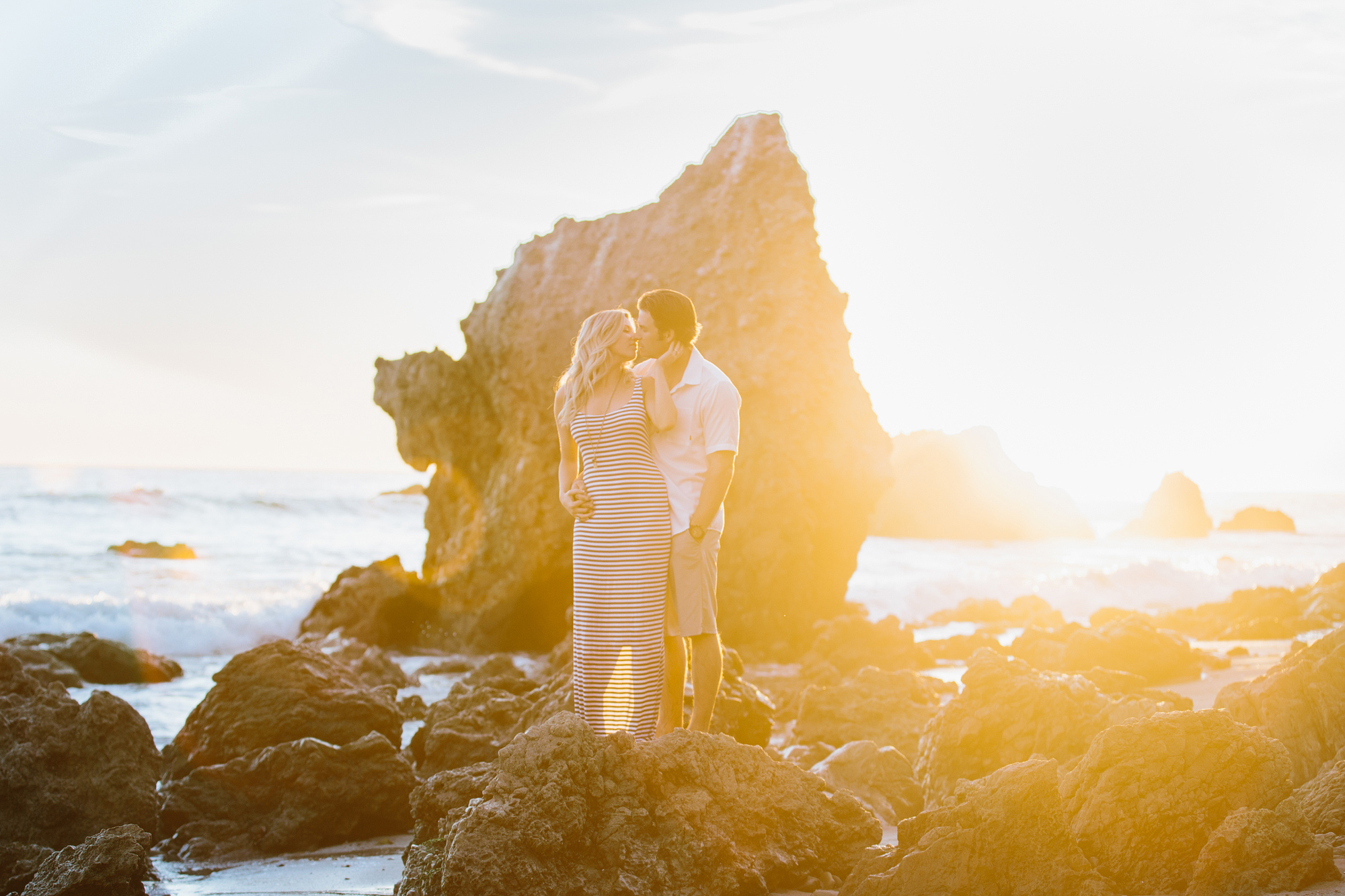 The couple standing int he midst of beach rocks. 